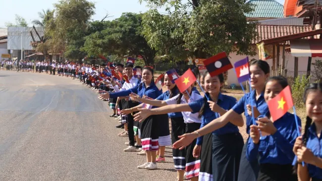 Rất đông thanh niên học sinh Lào đứng vẫy cờ chờ đón đoàn đua. Những tình cảm nồng hậu làm ấm lòng các vận động viên cũng như mỗi thành viên trong đoàn. Ảnh: Hoàng Lĩnh. 