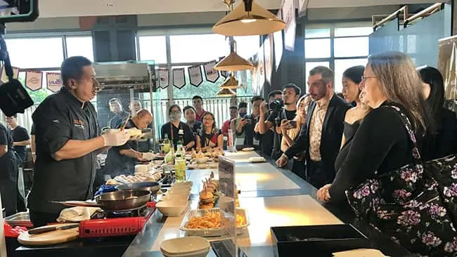 Tổng Lãnh sự Hoa Kỳ Marie C.Damour (đứng ngoài cùng mang túi hoa) cùng các chuyên gia đầu ngành trong lĩnh vực ẩm thực tại thành phố Hồ Chí Minh xem đầu bếp Chef Tristan Ngo chế biến món Burger tại sự kiện.