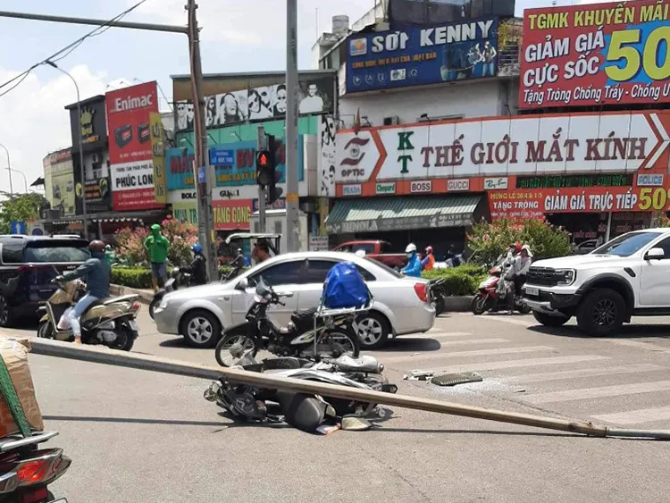 người phụ nữ đi xe gắn máy bị cột đèn đổ đè vào người và xe