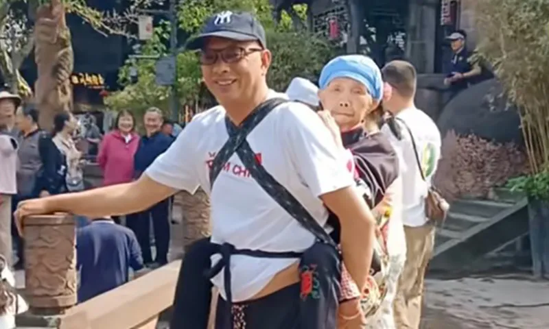 Người đàn ông cõng mẹ trên lưng bằng cái địu