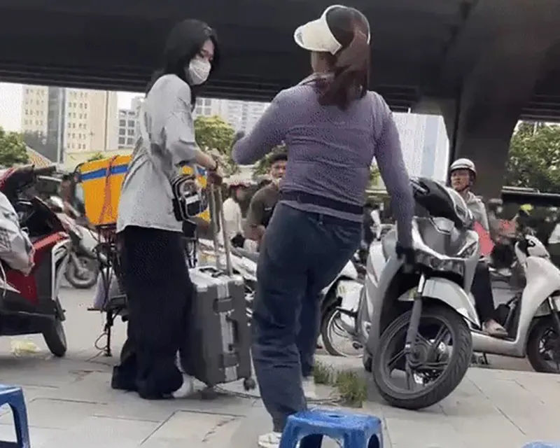 Bà bán hàng dùng chân đá vào vali của cô gái đứng đón xe trên vỉa hè Ảnh cắt từ clip