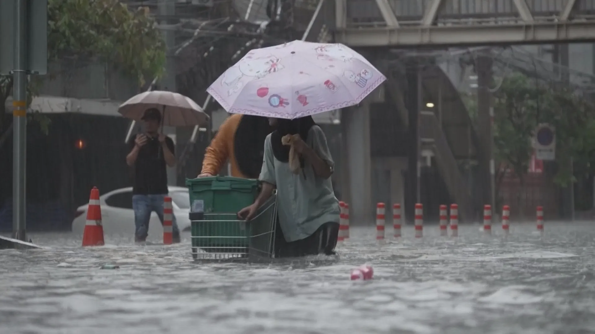 Người dân Bangkok lội nước ngập ngang đầu gối, che ô và đẩy xe hàng chở nhu yếu phẩm vượt qua một con phố bị bủa vây bởi dòng nước lũ đục ngầu sau hơn 24 giờ mưa lớn liên tục