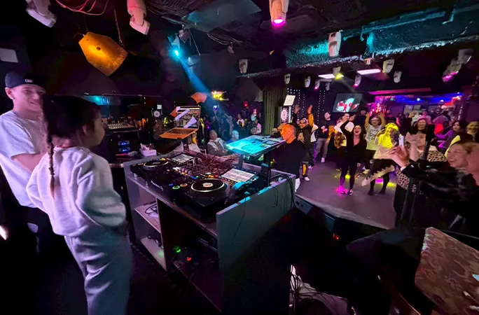 Illumi Maeda đứng trước bàn DJ tại câu lạc bộ