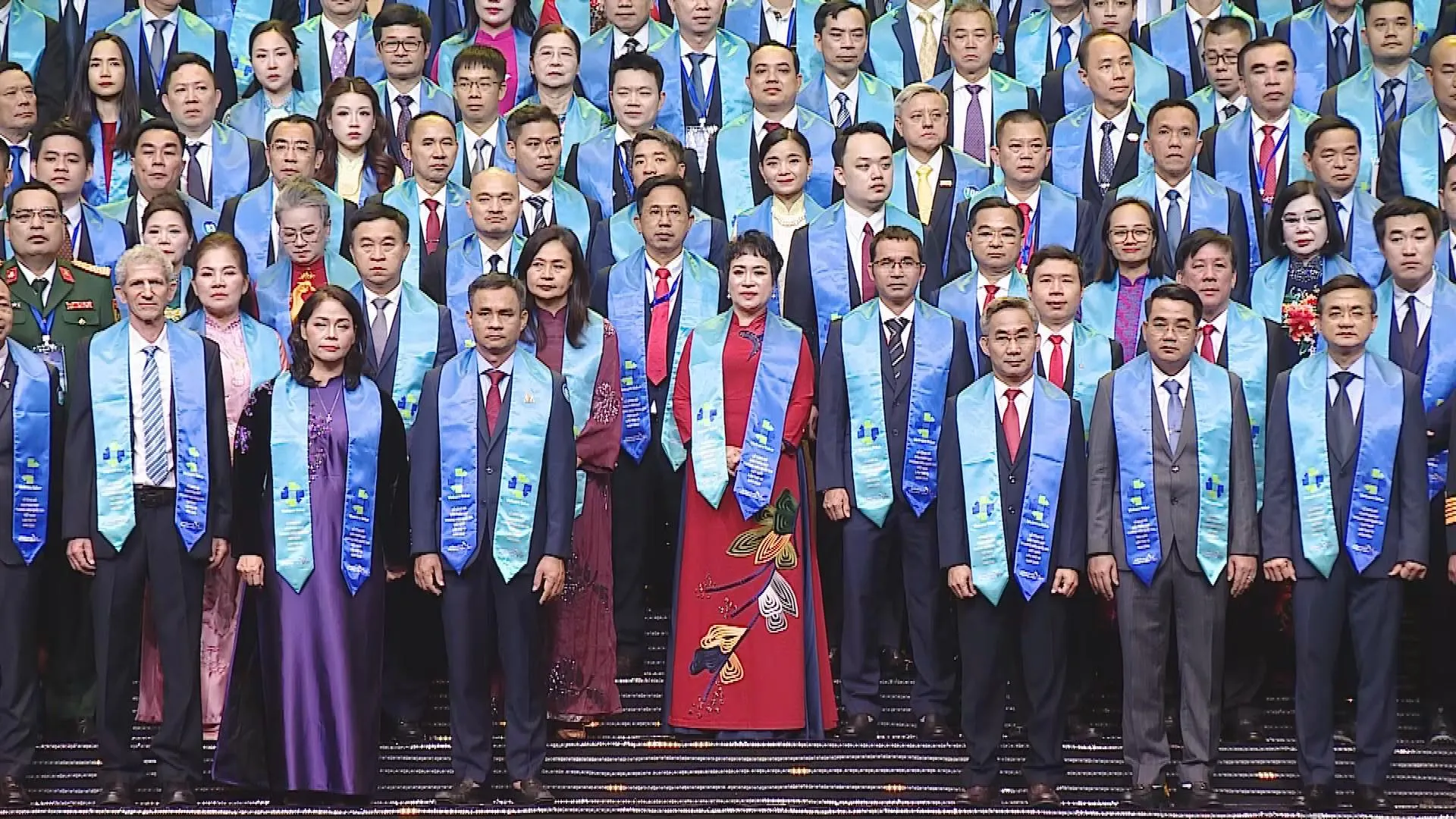 Toàn cảnh hàng đại biểu trong trang phục trang trọng, đeo dải băng xanh trên sân khấu. - Ảnh 1. Các doanh nhân đeo dải băng xanh tại sự kiện, ghi dấu sự ghi nhận đối với nỗ lực xây dựng thương hiệu Việt